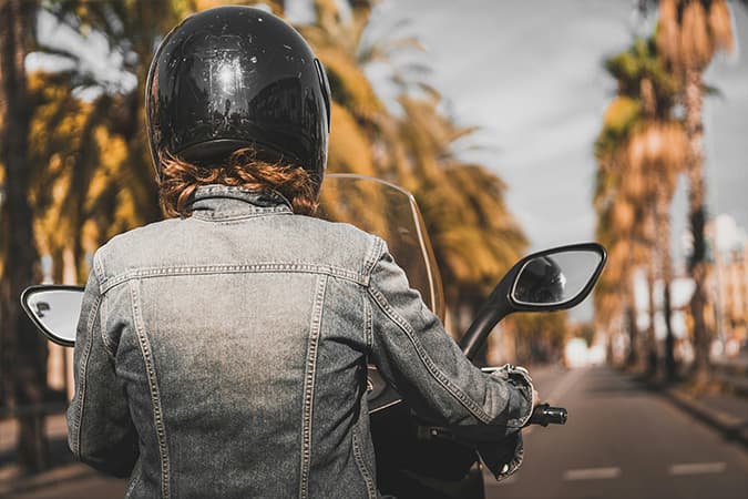 The back of a woman riding a motorbike down a palm-tree lined boulevard.
